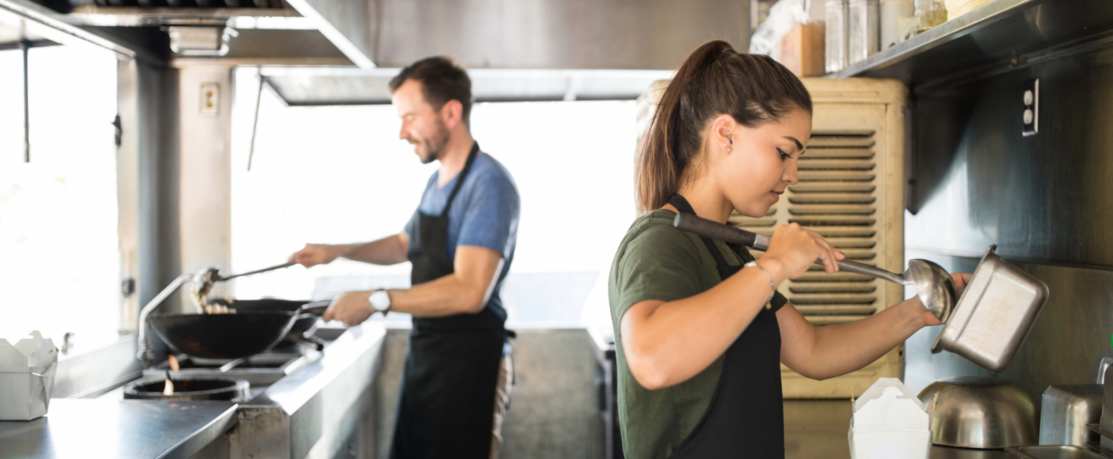 Man and woman prepare food truck fare in small commercial kitchen.